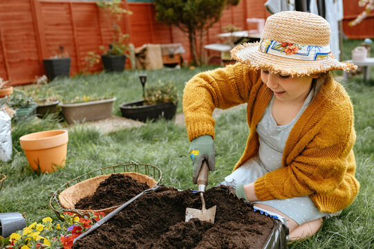 Smiling child scooping soil with garden trowel from container outdoors