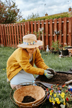 Child adding compost while planting flowers in garden container