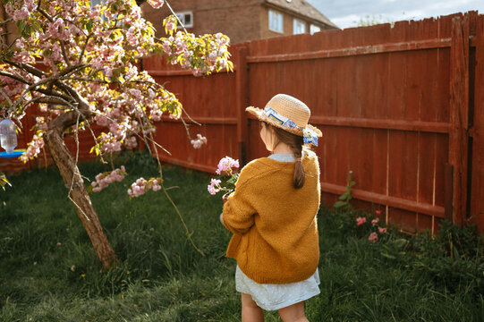 Girl carrying flowers standing near blooming tree in garden