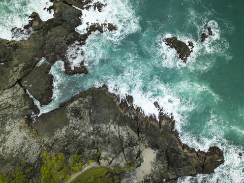 Aerial view of Siung Beach featuring turquoise waves crashing against dark volcanic rocks and white sea foam in Tepus, Special Region of Yogyakarta, Indonesia.