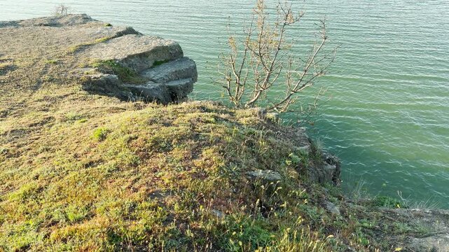 A flat, rocky plateau overlooks the calm green water of a large lake. This high viewpoint feels lonely and quiet. The gentle ripples on the water create a sense of deep peace.