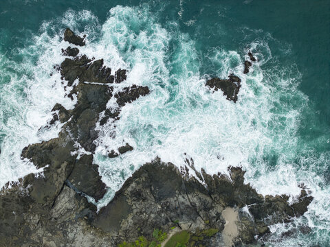 Aerial view of Siung Beach with turquoise waves crashing against dark volcanic rocks and white sea foam in Tepus, Special Region of Yogyakarta, Indonesia.