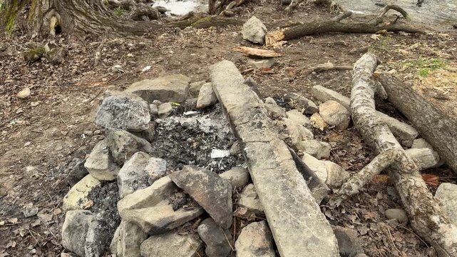 Cold grey ashes and burnt wood lie among large stones near a fast river. The empty fire pit creates a lonely and quiet feeling in the wild nature. It is a peaceful spot for a rest.