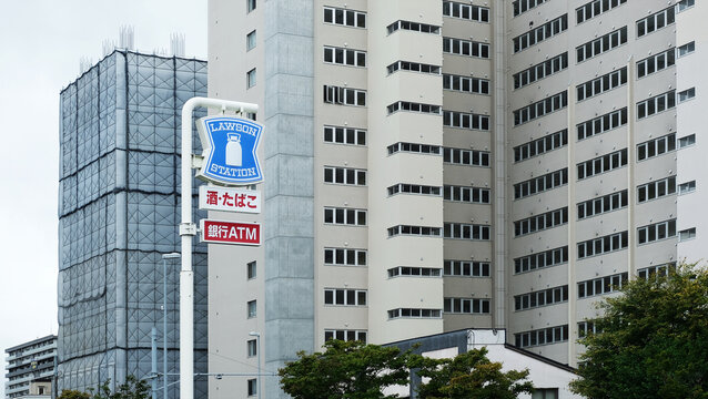 Sapporo, Japan on 26 September 2025: a Lawson sign at a street in Sapporo, Hokkaido. blue sign with white milk can logo, text below says "Alcohol, Tobacco" and "Bank ATM". tall apartment buildings sta