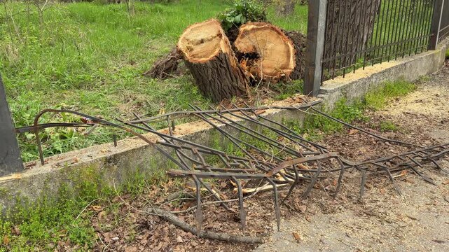 A heavy tree stump sits behind a broken iron fence on a grassy field. The scene feels chaotic and sad after the destructive impact. Sawdust covers the ground near the twisted metal.