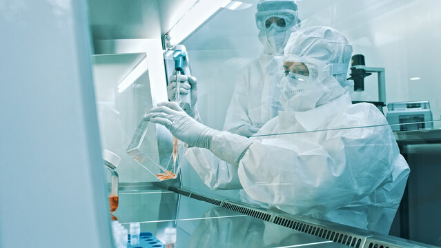 In a sterile laboratory, two researchers in clean suits meticulously handle microfluidic devices, advancing medical research in biotechnology.