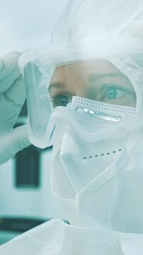 A female healthcare professional in full protective gear examines a sample in a sterile cleanroom, highlighting stringent protocols in the pharmaceutical industry to prevent illness transmission.