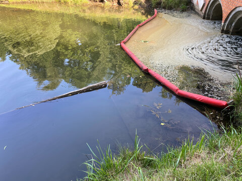 Containment boom holding back foam and pollution in river water near culvert.