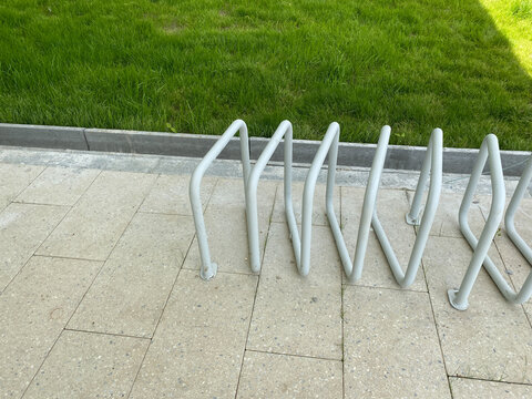 White metal bike stand located in public urban space. Minimalist bicycle parking furniture installed on tiled walkway with grassy background.