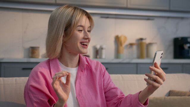 Happy smiling Caucasian teenage girl woman at home recording video smartphone social media stories greeting hello positive female vlogger blogger influencer chatting mobile phone distant call indoors