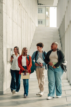 Group of diverse university students walking and talking on modern campus hallway, enjoying friendship and educational journey