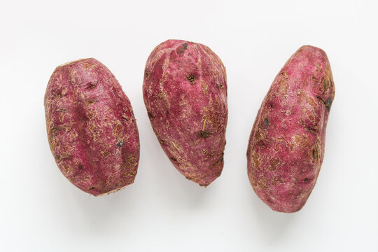 Three raw sweet potatoes, isolated on a clean white background.