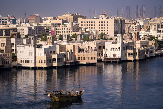 Aerial view of traditional wind towers and historic architecture along the waterfront with a wooden dhow boat on the water in Dubai, Dubai, United Arab Emirates.
