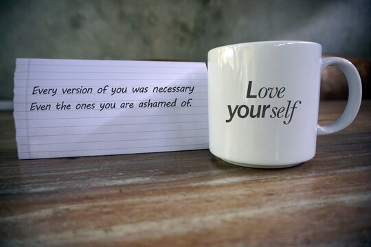 Inspirational motivational quote - Every version of you was necessary. Even the ones you are ashamed for. Love yourself. With text reminder on white empty cup and notepaper on the table. Self care.