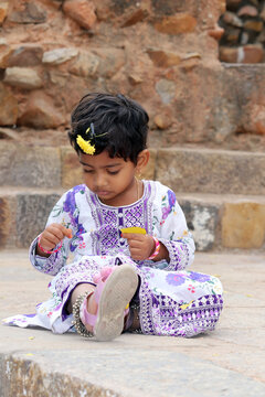 Young girl seated on stone steps, wearing a white and purple floral dress 
