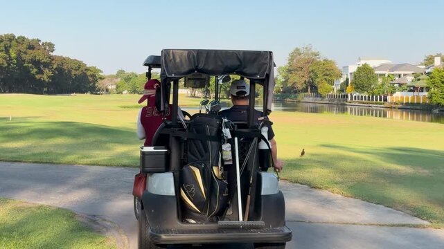 Asian Golfer and Caddy Driving a Golf Cart on a Fairway