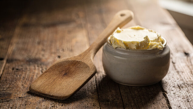Simple butter in a jar on a wooden surface with a spoon placed beside it