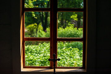 Fototapeta premium View through a rustic wooden window with a crucifix overlooking a green garden