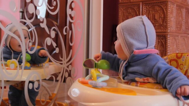 Baby in walker looking at reflection in the mirror, a baby sits in a baby walker and looks at himself with interest in a large mirror, the child's knowledge of the world and his first discoveries in a