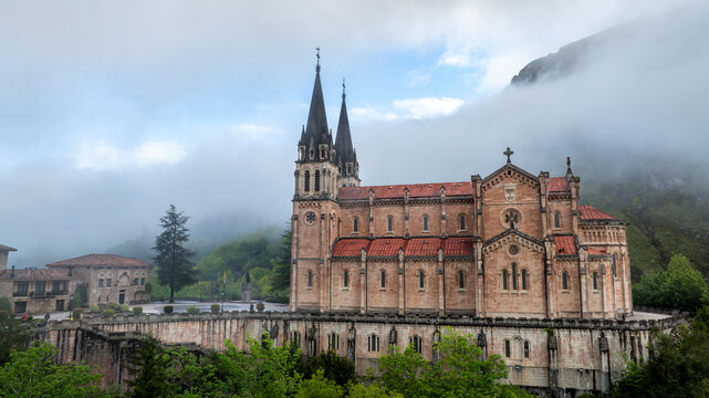 Aerial view of the majestic Basilica de Santa Maria la Real de Covadonga rises amidst swirling mists and verdant hills, its spires reaching towards the heavens, Cangas de Onis, Spain.