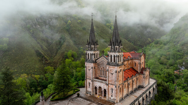Aerial view of the Basilica de Santa Maria la Real de Covadonga stands majestically against a backdrop of verdant mountains shrouded in mist, Cangas de Onis, Spain.