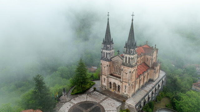 Aerial view of the Basilica de Santa Maria la Real de Covadonga emerges from the mist, its spires piercing the low-hanging clouds, Cangas de Onis, Spain.