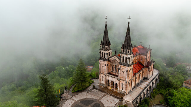 Aerial view of the Basilica de Santa Maria la Real de Covadonga emerges majestically through swirling clouds, a testament to timeless beauty, Cangas de Onis, Spain.