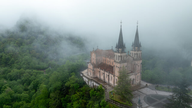 Aerial view of basilica piercing the misty heights, its gothic spires a stark contrast to the lush green forest, Basilica de Santa Maria la Real de Covadonga, Cangas de Onis, Spain.
