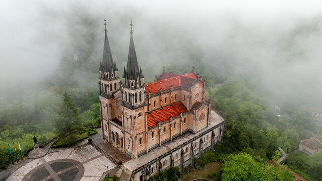 Aerial view of the Basilica de Santa Maria la Real de Covadonga rises majestically, its spires piercing through the ethereal mist that clings to the verdant hills, Cangas de Onis, Spain.