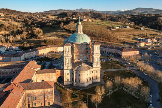 Aerial view of the Santuario di Vicoforte featuring its massive elliptical dome and surrounding porticoed buildings under golden hour light in Vicoforte, Piedmont, Italy.