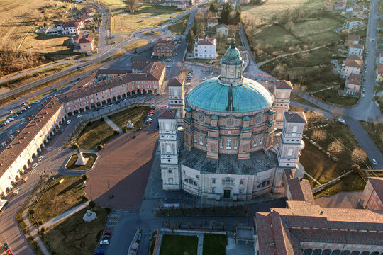 Aerial view of the Santuario di Vicoforte featuring its massive elliptical green dome and surrounding historic buildings under soft sunlight in Vicoforte, Piedmont, Italy.