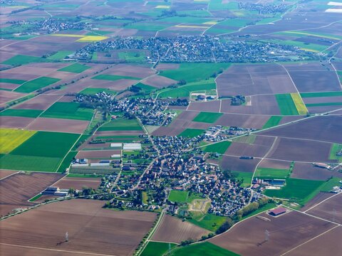 Aerial view of a patchwork of green and brown agricultural fields surrounding quaint villages, Wintzenheim-Kochersberg, Grand Est, France.