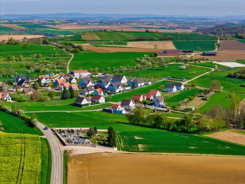 Aerial view of a village with colorful rooftops surrounded by vibrant green fields and brown earth, Wintzenheim-Kochersberg, Grand Est, France.