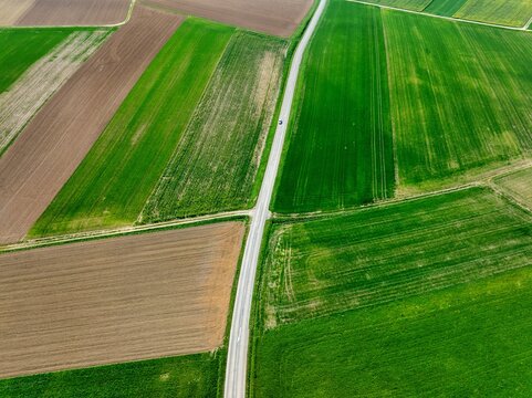 Aerial view of a striking mosaic of vibrant green fields and earthy brown plots intersected by a straight grey road, Wintzenheim-Kochersberg, Grand Est, France.
