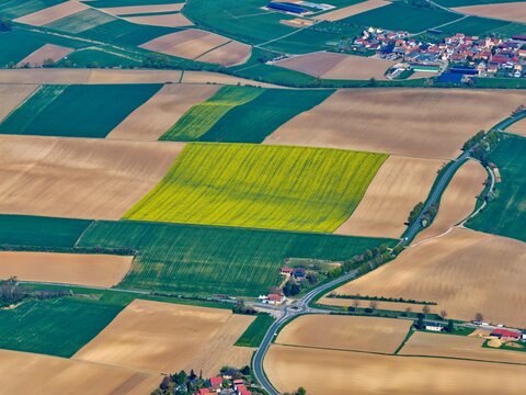 Aerial view of a captivating patchwork of golden fields and verdant crops unfolds, bisected by winding roads near quaint settlements, Wintzenheim-Kochersberg, Grand Est, France.