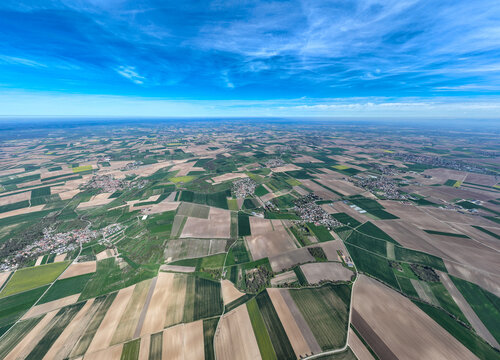 Aerial view of a patchwork of agricultural fields stretching under a bright blue sky with scattered clouds, Wintzenheim-Kochersberg, Grand Est, France.
