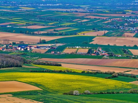 Aerial view of a vast, colorful patchwork of golden and green fields, dotted with villages and distant hazy hills, Wintzenheim-Kochersberg, Grand Est, France.