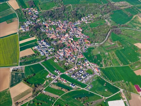 Aerial view of patchwork fields meet the clustered rooftops of a quaint village nestled amidst verdant trees, Wintzenheim-Kochersberg, Grand Est, France.