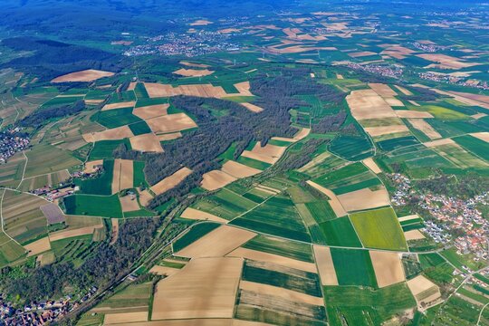 Aerial view of a vibrant patchwork of emerald and golden fields, dense forests, and scattered villages, Wintzenheim-Kochersberg, Grand Est, France.