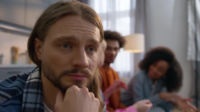 Despair Caucasian man at home worry thinking depressed male having panic attack feeling ignored while multiethnic African American friends talk together social exclusion anxiety mental health problem