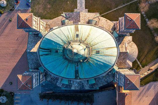 Aerial view of the Santuario di Vicoforte featuring its massive elliptical copper dome and four corner towers during golden hour in Vicoforte, Piedmont, Italy.