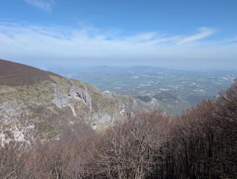   
Panorama montano con pendii rocciosi, un&rsquo;ampia vallata che si apre in lontananza sotto un cielo limpido. Una scena naturale ampia e luminosa