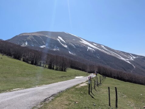   
Paesaggio montano con pendii boscosi in ombra e una vetta pi&ugrave; alta illuminata dal sole, con tracce di neve e cielo limpido. Un&rsquo;atmosfera luminosa e naturale