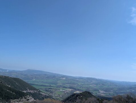   
Panorama montano con pendii rocciosi, un&rsquo;ampia vallata che si apre in lontananza sotto un cielo limpido. Una scena naturale ampia e luminosa