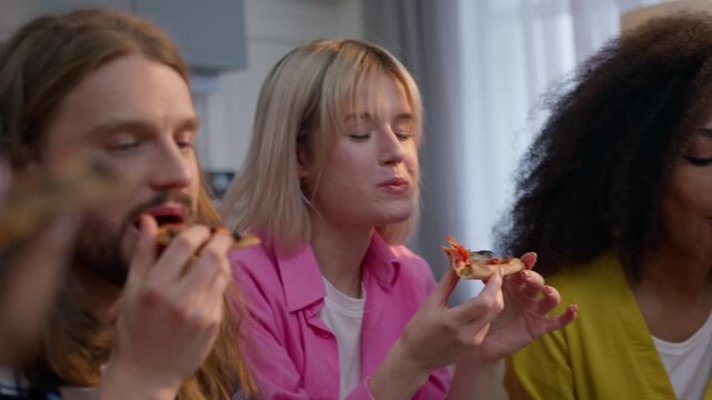 Four multiracial friends men women enjoying party at home eating pizza drinking beer and cider Caucasian woman African American man girls and guys fast food delivery friendship having fun bad habit