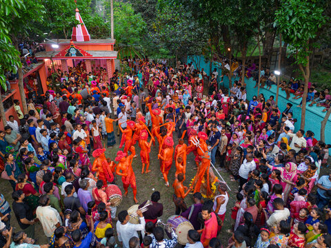 Munshiganj, Bangladesh - 13 April 2026: Aerial view of vibrant orange-clad performers captivating a dense crowd near a distinct pink-roofed temple, amidst verdant foliage.