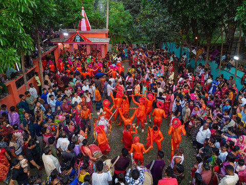 Munshiganj, Bangladesh - 13 April 2026: Aerial view of a vibrant festival, energetic orange-clad performers amidst a dense crowd, near a colorful temple.