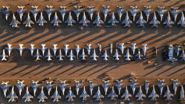 Tucson, United States - 06 February 2025: Aerial view of rows of dormant grey military jets, their metallic bodies contrasting with long, dark shadows on the sun-baked desert floor.