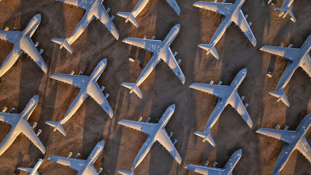 Tucson, United States - 06 February 2025: Aerial view of a vast boneyard of retired aircraft, their stark white bodies casting long, dramatic shadows across the sun-baked desert floor.