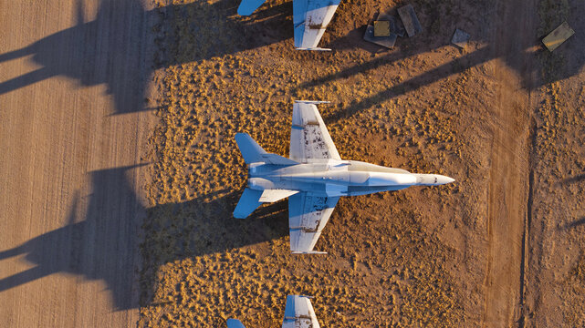 Tucson, United States - 06 February 2025: Aerial view of military fighter jets parked on the arid, golden desert ground, their stark forms casting long, dramatic shadows.